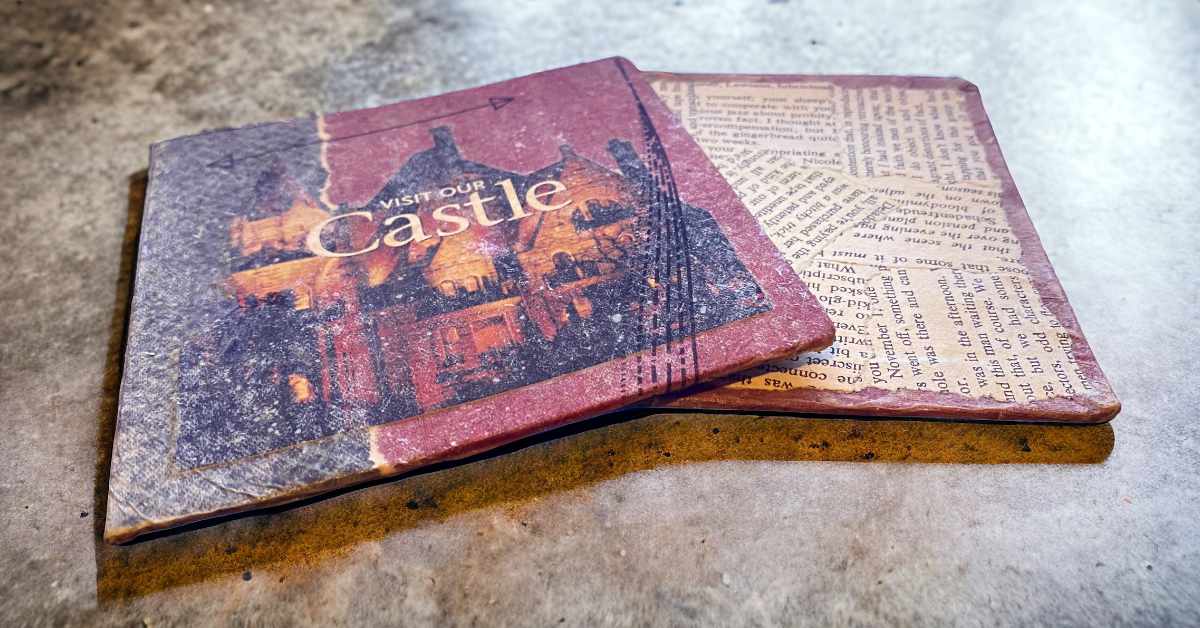 This image displays two handcrafted book covers laid on a textured surface, intended to be bound into a journal. The cover on top features an illustration of a castle with warm tones and the text "VISIT OUR CASTLE," suggesting a vintage or nostalgic theme. The second cover, partly visible beneath the first, is covered in text, implying it may be repurposed from a printed document or book page. The aged appearance of both covers, with their distressed edges and muted colors, contributes to a rustic and artisanal aesthetic.