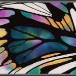 The image shows a workspace in digital art software. The artwork in progress is an abstract close-up of a butterfly wing with thick black outlines dividing various sections. These sections are filled with vibrant, watercolour-like gradients in shades of teal, blue, purple, orange, yellow, and pink. The interface displays a variety of tools and settings on both sides of the screen, including brush types, colour palettes, layer controls, and opacity sliders. The left panel focuses on drawing and painting tools, while the right panel includes layer management and colour selection.