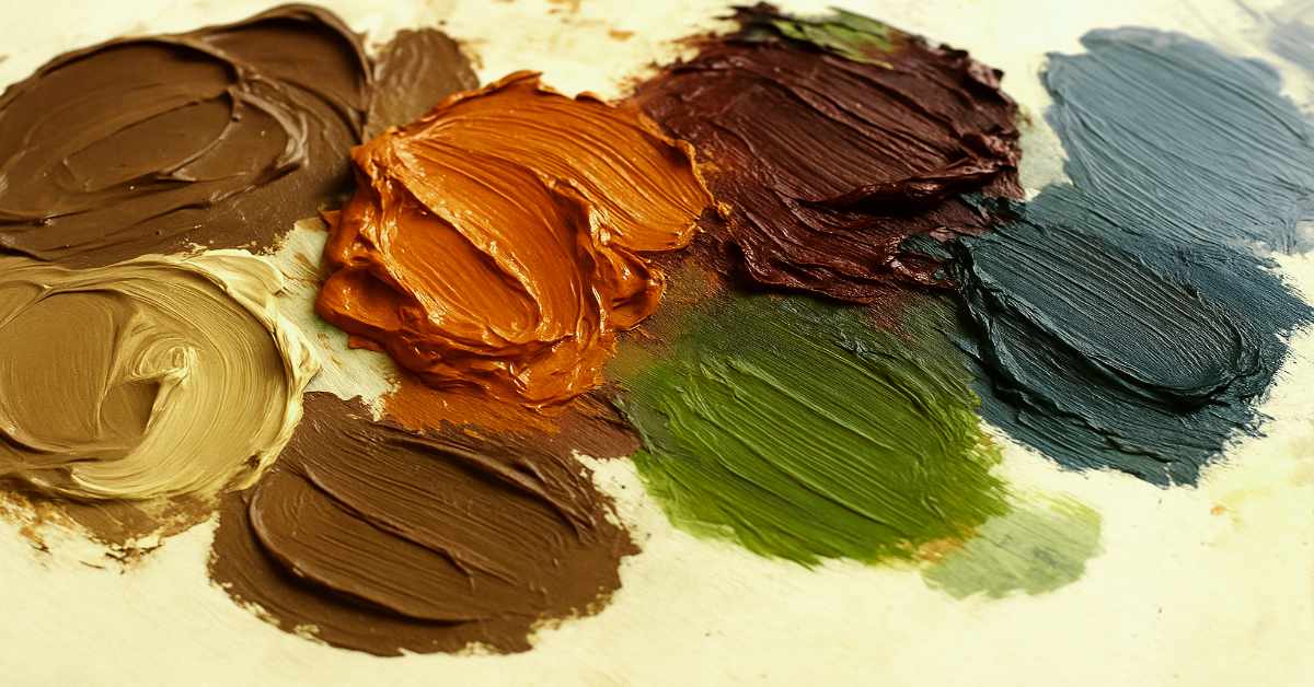 A close-up photo of thick, textured blobs of oil paint in earthy and autumn-inspired tones arranged on a light-colored palette. The colors closely resemble the October 2025 palette, including dark brown, burnt orange, burgundy, beige, green, and blue-gray hues, with visible brush strokes adding texture and depth.
